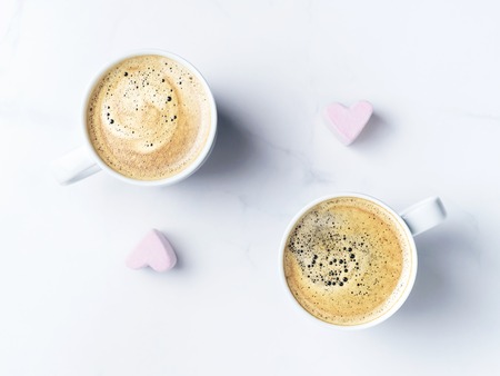 Romantic desk top with two cups of coffee and pink heart shaped marshmallows. Top view. Copy space.の写真素材