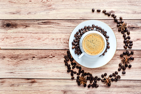 Top view of a cup of hot coffee on wooden rustic table with spilled coffee beans and anise. Space for text .の写真素材