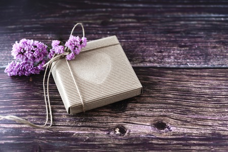 Handmade gift concept. Craft paper recycle gift box with flowers on wooden table. Rustic style. Copy space.の写真素材