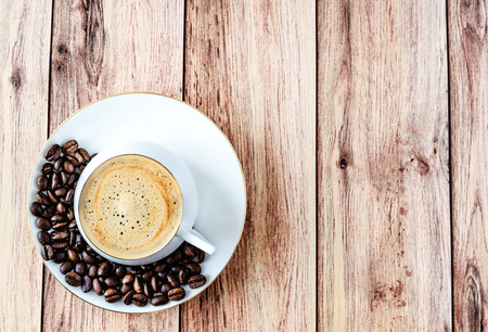 Top view of a cup of hot coffee on wooden rustic table with spilled coffee beans. Space for text .の写真素材