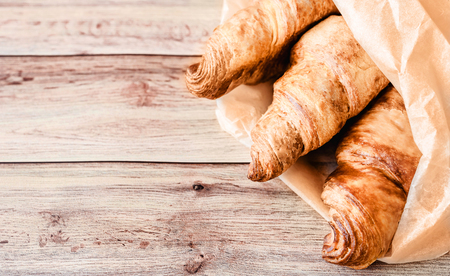 Three delicious croissants wrapped in baking paper on wooden table. Top view. Copy space.の写真素材
