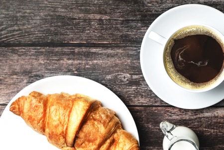 Perfect breakfast of croissant and coffee with milk on wooden table. Rustic style. Top view.の写真素材