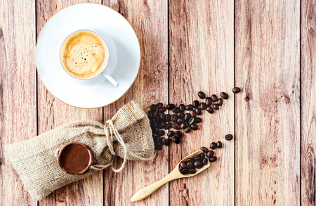 Top view of a cup of hot coffee and coffee beans in a wooden scoop and spilling out from a hessian bag on wooden rustic table. Space for text .の写真素材