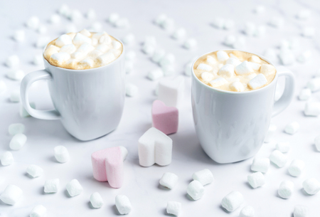 Romantic cozy desk top with two cups of coffee with heart shape marshmallows on marble table.の写真素材