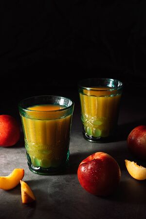 Still life of fresh delicious sweet nectarines with droplets of water and juice in turquoise vintage glasses on dark background. Low key.の写真素材
