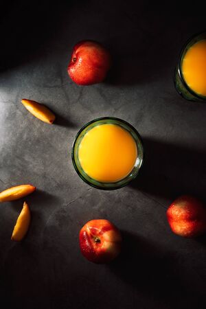 Still life of fresh delicious sweet nectarines with droplets of water and juice in turquoise vintage glasses on dark background. Low key. Top view.の写真素材