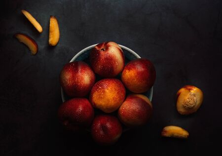 Still life of fresh delicious sweet nectarines with droplets of water in a bowl on dark background. Low key. Top view.の写真素材