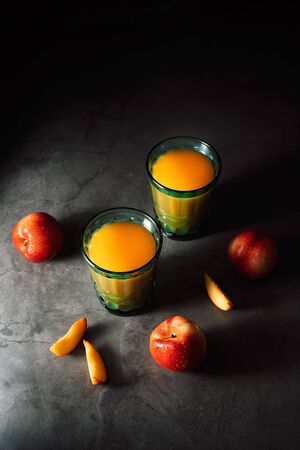 Still life of fresh delicious sweet nectarines with droplets of water and juice in turquoise vintage glasses on dark background. Low key.の写真素材