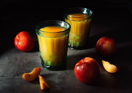 Still life of fresh delicious sweet nectarines with droplets of water and juice in turquoise vintage glasses on dark background. Low key.の写真素材