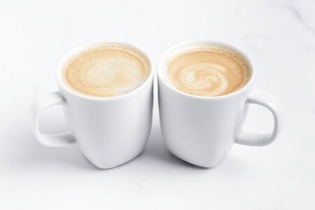 Minimal desk top with two white cups of coffee on marble table. Close-up. Space for text .の写真素材