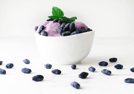 Ice-cream decorated with fresh berries of a honeysuckle and green leaves on white background. Close-up.の写真素材