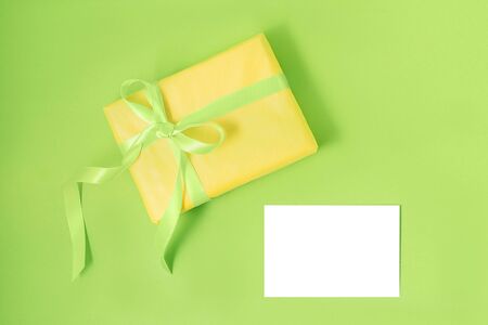 Yellow gift box with green silk ribbon and empty isolated label on pastel green background. Holiday gift concept. Flat lay. Copy space.の写真素材