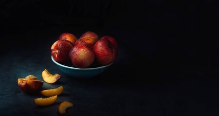 Still life of fresh delicious sweet nectarines with droplets of water in a bowl on dark background. Low key. Place for text.の写真素材