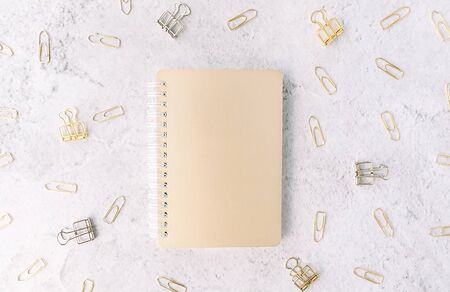 Closed gold notepad on background with set of silver and gold paper clips on light grey cement surface. Flat lay. Office and business concept.の写真素材