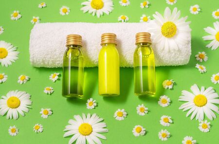 Flat lay of small mockup bottles with spa cosmetic products on green background with fresh camomile blossoms. Women beauty and beauty salon cosmetics concept. Eco concept.の写真素材