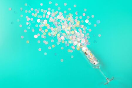 Round multicolored confetti poured out of champagne glass on trendy mint background. Flat lay style. Celebration concept. Copy space.の写真素材