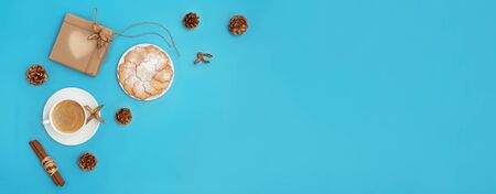 Trendy Christmas background of coffee, ginger cookies, craft gift box and golden cones on cyan blue backdrop. Holiday season concept. Web banner. Flat lay style.の写真素材