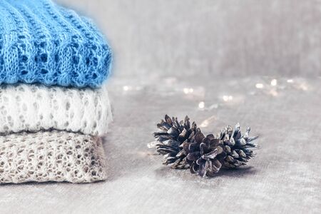 Stylish knitted pastel colored sweaters and one in trendy blue color folded in stack with pine cones...