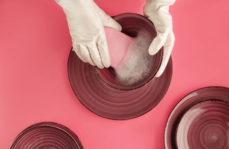 emale hands in pearly white gloves washing beautiful ceramic plates on trendy pink background. Household chores concept. Backdrop for your design. Flat lay style. Copy space.の写真素材