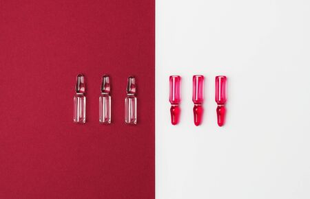 Line of ampules for injections with red and transparent liquid on isolated white and dark red...