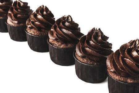 Delicious chocolate cupcakes with gold sparkles sprinkled on chocolate icing lined up diagonaly on isolated white background. Mockup for your design. Close-up. Place for text.の写真素材