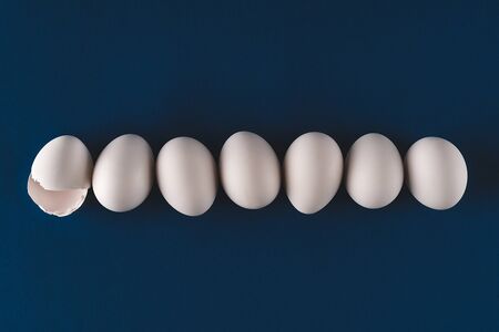 Abstract background of white eggs lined up on trendy dark blue backdrop. Easter concept. Dark and...