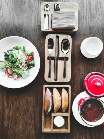 Vegetable spring salad on white porcelain plate and soup in red pot on textured wooden table in cafe with modern trendy interior. Mockup for your design. Flat lay style.の写真素材