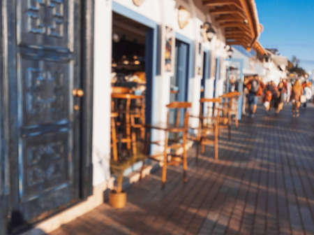 Seafront mediterranean cafe with white walls, beautiful deep blue wooden doors and light blue windows in setting sun. Summer vacation. Defocused background. Travel concept.の写真素材