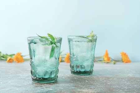 Two beautiful vintage turquoise glasses with cold drink and ice cubes, with fresh green mint leaves...