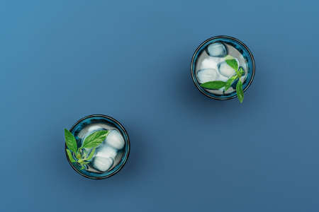 Two beautiful vintage blue glasses with cold drink and ice cubes, with fresh green mint leaves on...