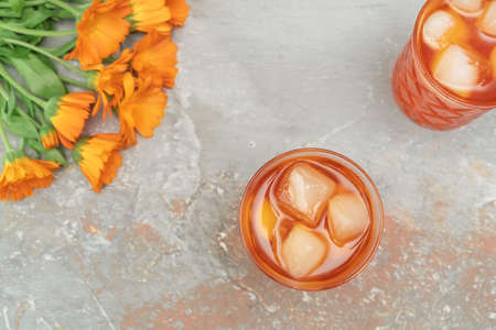 Orange cocktail in vintage crystal glasses with marigold flower bouquet on natural stone background....