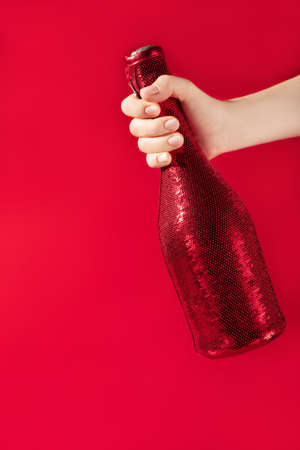 Modern design template with female hand holding champaigne bottle covered in red sequines on red background. Christmas background concept. Holiday celebration concept. Modern template for your design.の写真素材