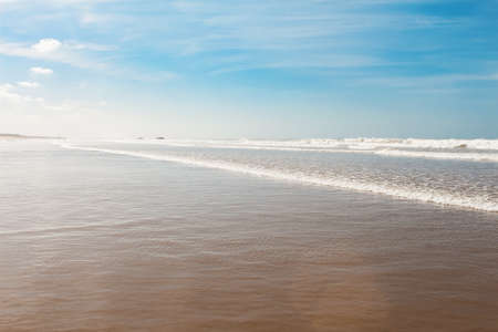 View over sandy beach of Atlantic ocean with waves coming in perfect parallel lines on a bright...