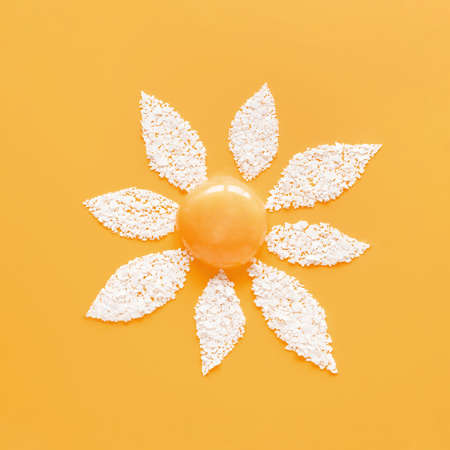 Flower made of yolk and cracked egg shell in abstract style on soft yellow background. Organic meal...