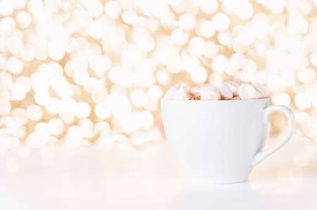 Gift card with white cup of coffee and marshmallow on golden background of christmas lights bokeh. Mockup for decorative design. Christmas and New Year concept. Copy space.の写真素材