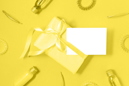 Gift box with silk ribbon and hair accessories in trendy yellow color and empty isolated label. Holiday gift concept. Flat lay style. Color 2021 concept. Copy space.の写真素材
