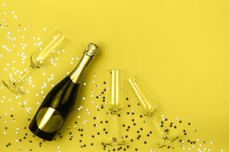 Champagne bottle and glasses with shiny star shaped confetti and party streamers toned in trendy yellow color. Holiday concept. Color 2021 concept. Flat lay style. Mockup for your design. Copy space.の写真素材