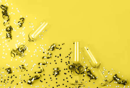 Champagne glasses with shiny star shaped confetti and party streamers toned in trendy yellow color. Holiday concept. Color 2021 concept. Flat lay style. Mockup for your design. Copy space.の写真素材