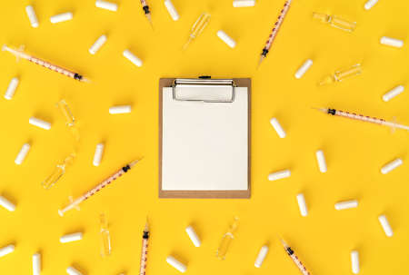 Blank medical clipboard, syringes and ampoules with transparent liquid on trendy yellow background. Cosmetology and medicine background.  virus vaccine concept. Flat lay style.の写真素材
