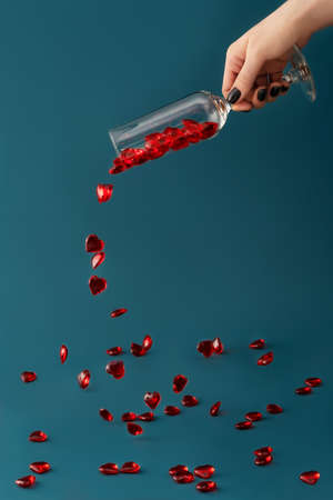 Beautiful card with female hand pouring red hearts from champagne glass on dark aqua backdrop. Love and celebration concept. Great design for any purposes. Closeup.の写真素材