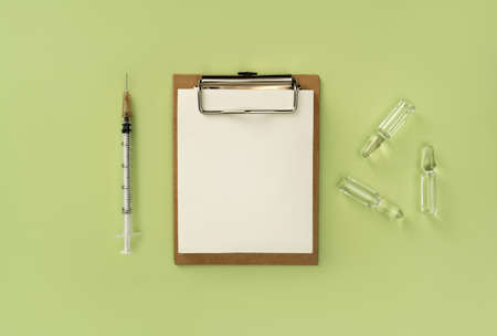 Blank medical clipboard, syringe and ampoules with transparent liquid on green background. Natural medicine background.  virus vaccine concept. Flat lay style.の写真素材