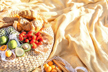Picnic basket with fruit, vegetables and croissant. Picnic on yellow plaid on sunny meadow background. Copy space. Lifestyle concept. Food and drinks concept.の写真素材