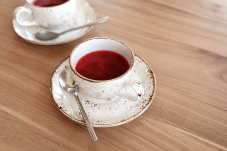 Red fruit tea in trendy ceramic white cups with brown decor on wooden table. Food background in...