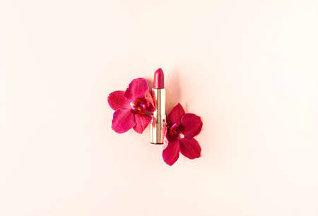 Decorative cosmetics composition of lipstick decorated with orchid flowers on pastel pink background. Natural cosmetics concept. Flat lay style. Copy space.の写真素材