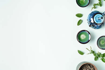 Green tea in a dark blue clay teapot and small cups on pastel blue background with mint leaves decoration. Tea ceremony concept. Copy space, top view. Flat lay style. Creative minimalist layout.の写真素材