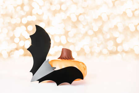 Halloween background with cake in a form of pumpkin decorated with black plastic bat on golden backdrop of holiday lights bokeh. Halloween celebration concept. Copy space.の写真素材