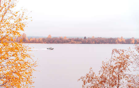 Beautiful autumn misty lake with motorboat and forest wild landscape. Autumn forest and lake background. Great design for any purposes.の写真素材