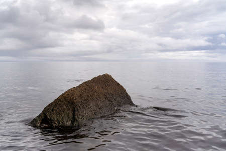 Beautiful autumn misty grey lake with rocky shore and cloudy sky at sunset. Dark and moody nature background. Great wallpaper design. Copy space.の写真素材