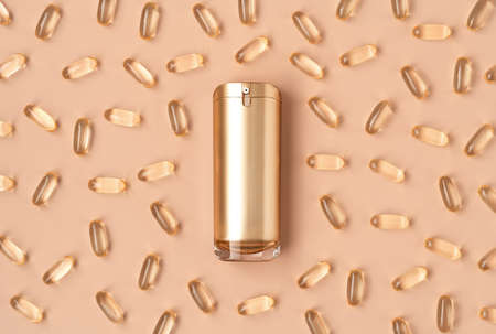 Beautiful composition of gold mockup cosmetic bottle and vitamin capsules on pastel background. Natural anti-ageing cosmetics concept in trendy colors. Creative trendy cosmetics flat lay. Copy space.の写真素材