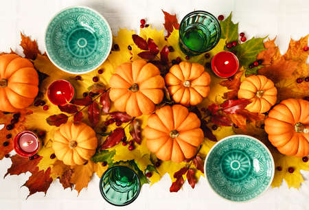 Mockup green vintage plates and glasses, maple leaves, pumpkins, cranberries and candles on white tablecloth background. Autumn composition in flat lay style. Halloween and thanksgiving concept.の写真素材